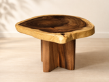 A rustic live-edge wooden stool with a thick, irregularly shaped top showing natural wood grain and a live edge, supported by three sturdy block legs, set against a neutral beige background.