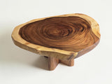 A rustic live-edge wooden stool or coffee table with a natural tree slice top and three short legs, shown on a clean white background.