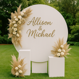 White ripple round backdrop with gold script 'Allison & Michael' sign, styled with dried florals and plinths on green garden lawn