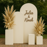 Triple ripple arch panel with neutral dried floral styling and plinths, displayed outdoors on brick paving for wedding decor