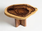 A rustic live-edge wooden table with a thick, irregularly shaped top showing natural wood grain patterns and a single carved wooden leg, photographed on a clean white background.