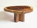 A rustic live-edge wooden table with a thick, polished slab top showing natural wood grain patterns and a three-leg pedestal base, set against a plain white background.