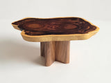 A rustic live-edge wooden table with a dark brown and black grain top and light tan edges, supported by three chunky wooden legs, shown on a plain white background.
